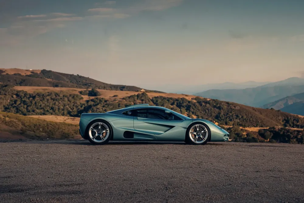 {"fr":"McLaren F1 1990s bleu sur route montagneuse avec paysage de collines verdoyantes.","nl":"Blauwe McLaren F1 uit de jaren 90 op bergweg met groene heuvels op achtergrond."}