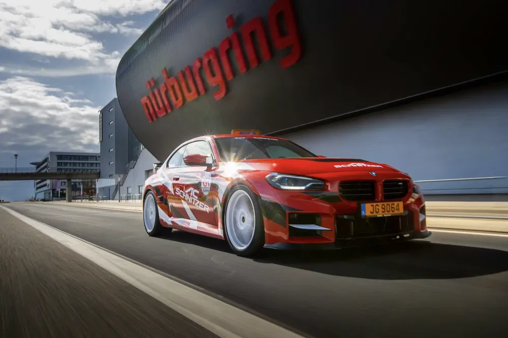 BMW de course rouge sur la piste Nürburgring, virage rapide avec arrière-plan du circuit.