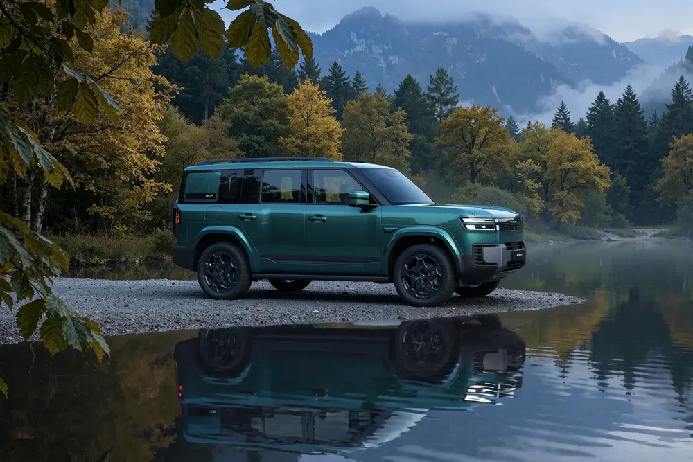Groene SUV geparkeerd bij meer, omgeven door herfstbos en bergen.