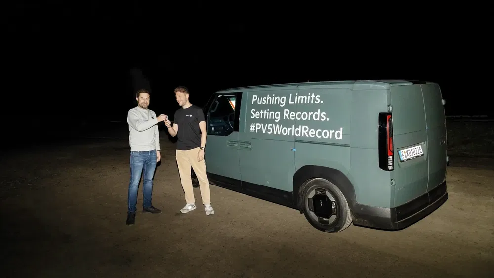 Fourgon électrique avec slogan record, deux hommes se serrent la main la nuit.