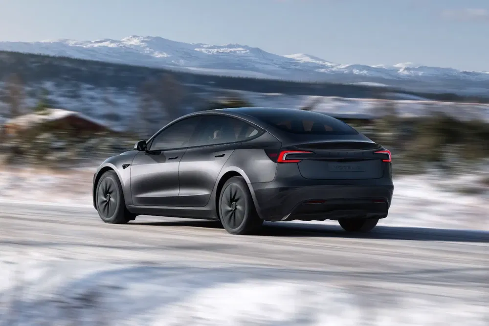 Tesla Model 3 roulant sur une route enneigée avec des montagnes en arrière-plan.