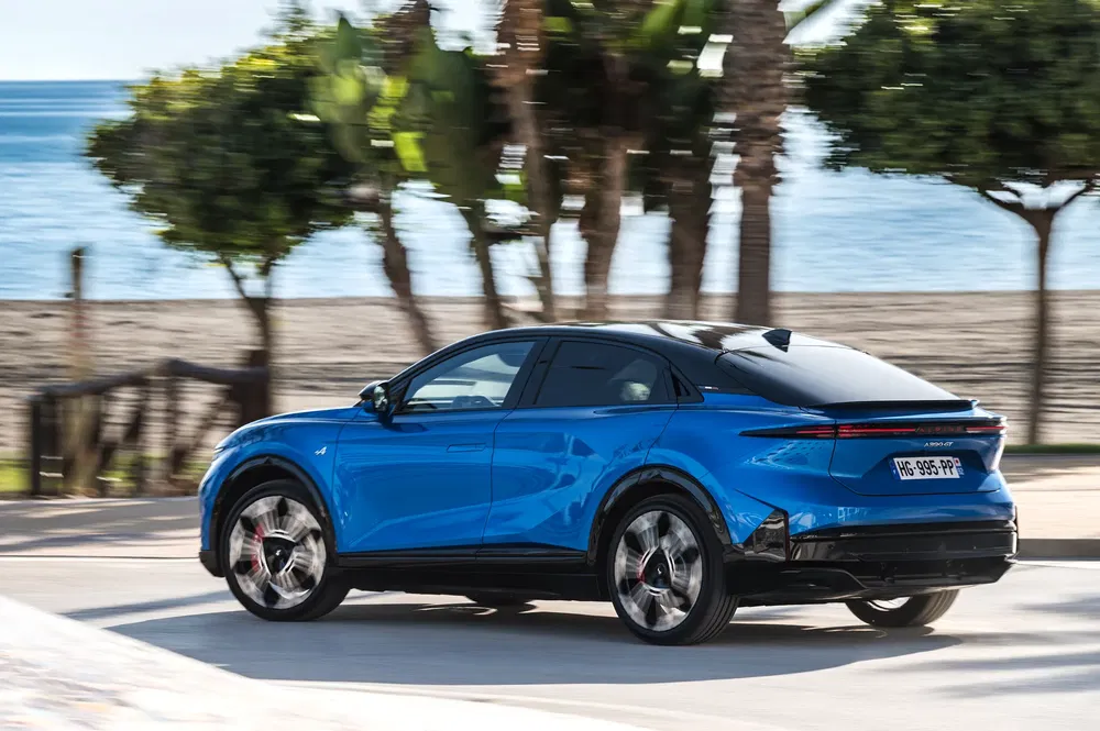 Peugeot 408 bleu électrique roulant sur une route côtière ensoleillée avec palmiers.