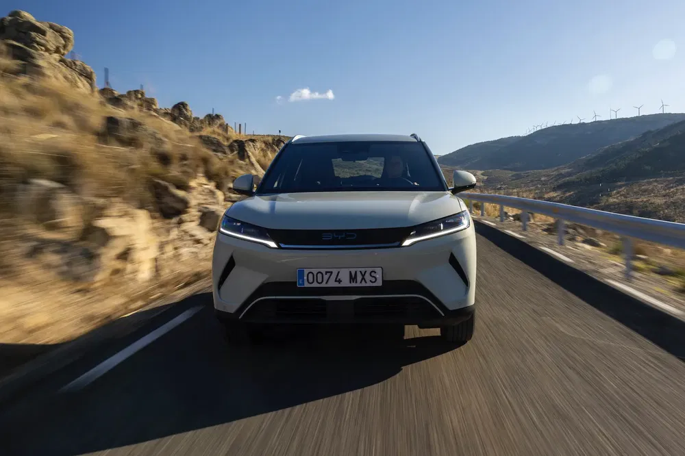SUV BYD en mouvement sur route de montagne, ciel clair et éoliennes en arrière-plan.