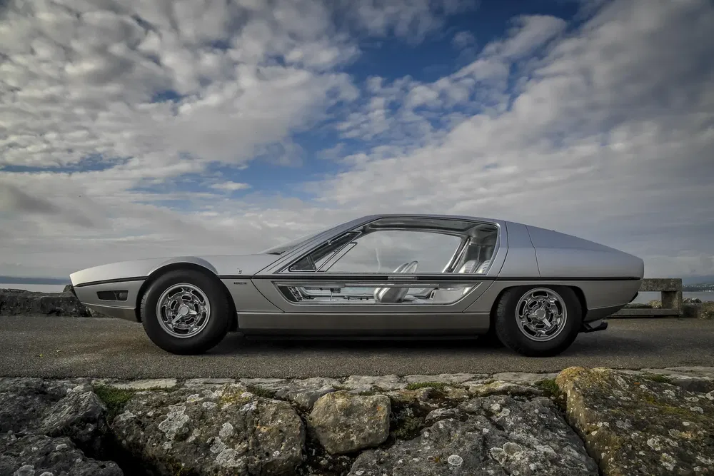 Maserati Boomerang conceptauto uit de jaren '70 geparkeerd op een rotsachtige weg met bewolkte lucht.