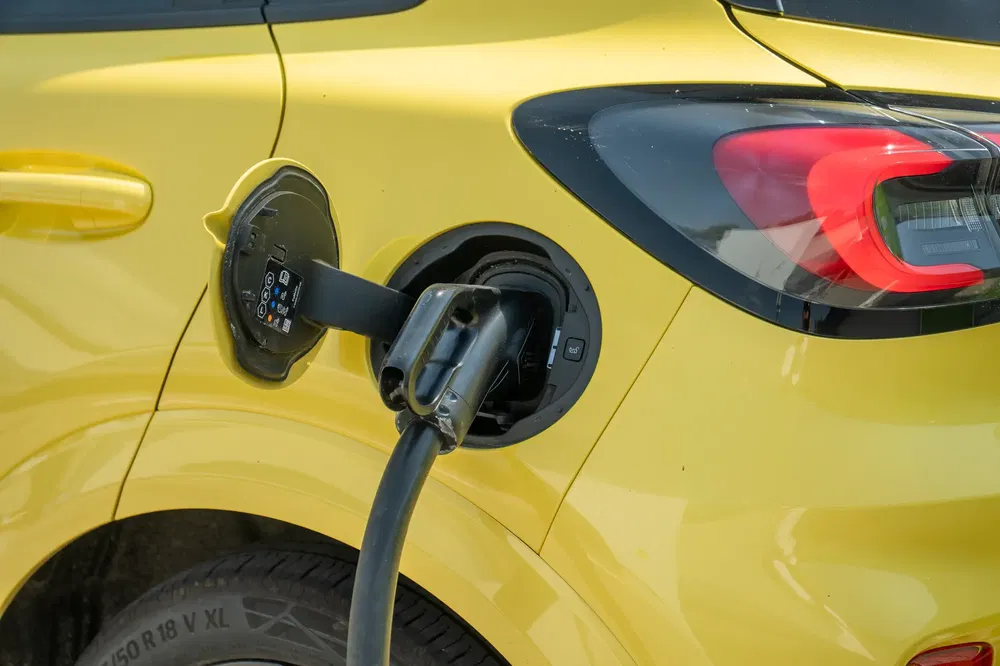 Geel elektrische auto wordt opgeladen; kabel aangesloten op achterport.