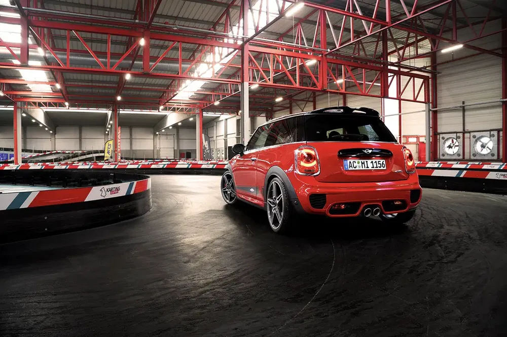 Mini Cooper rouge sur circuit de karting intérieur avec éclairage industriel.
