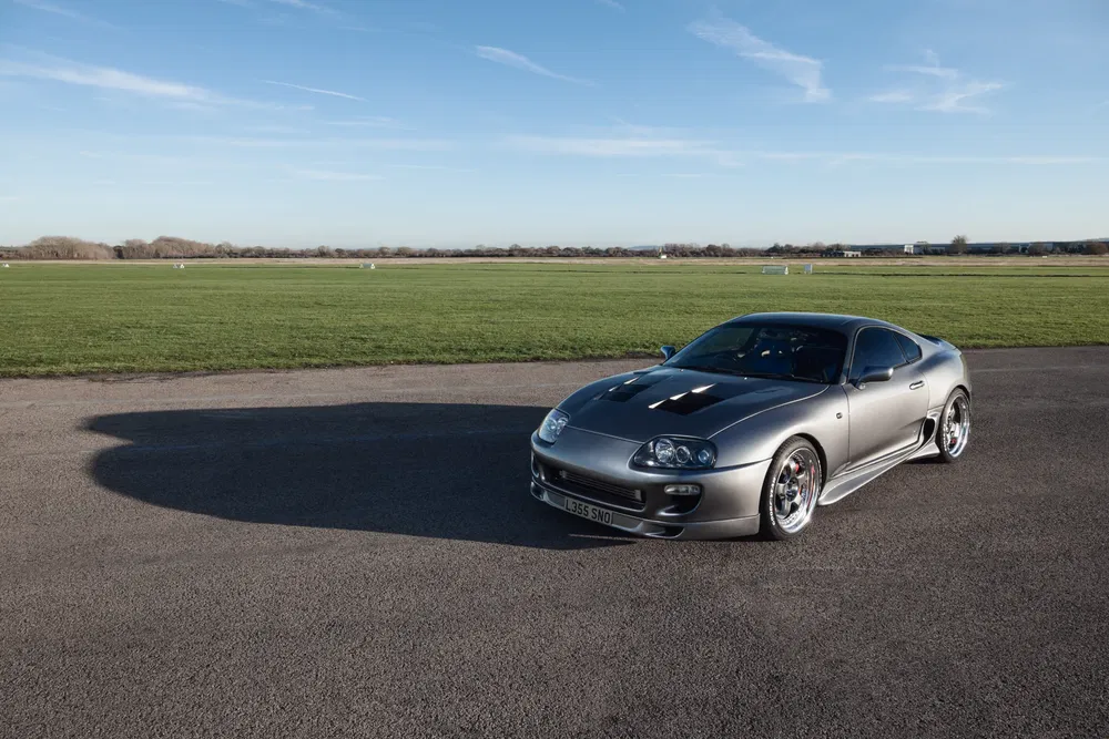 Voiture Toyota Supra grise sur piste d'atterrissage par journée ensoleillée.