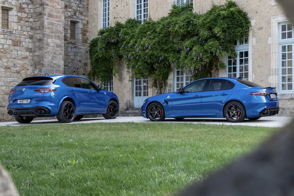 Blauwe Alfa Romeo Stelvio en Giulia Quadrifoglio geparkeerd voor een historisch gebouw.