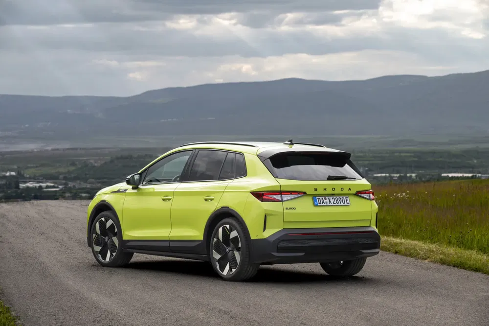 Felgele Skoda Enyaq iV elektrische auto op panoramische weg onder bewolkte hemel.