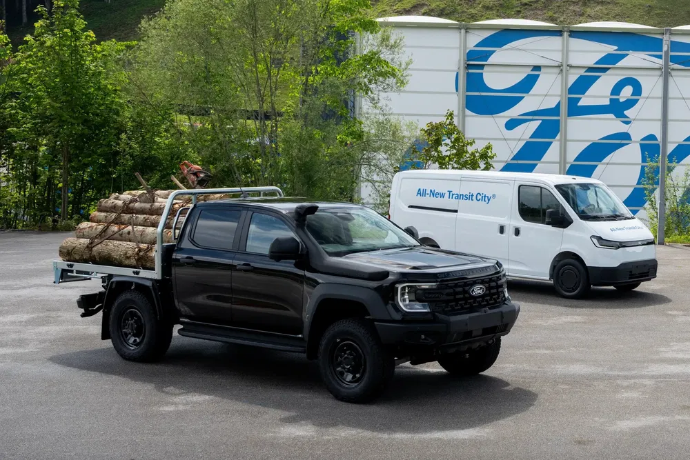 Pick-up Ford noir transportant des rondins, devant une camionnette All-New Transit City blanche.