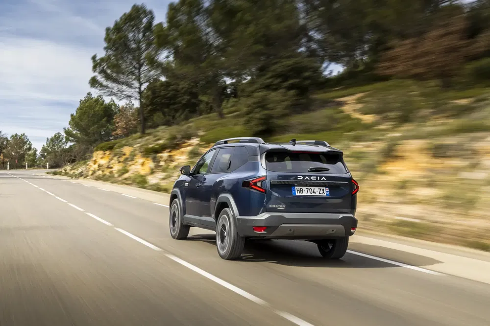Blauwe Dacia Duster rijdt op een landelijke weg omgeven door bomen.