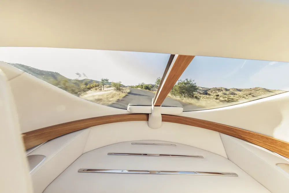Intérieur luxueux de voiture avec bois et cuir blanc, vue panoramique sur route déserte.