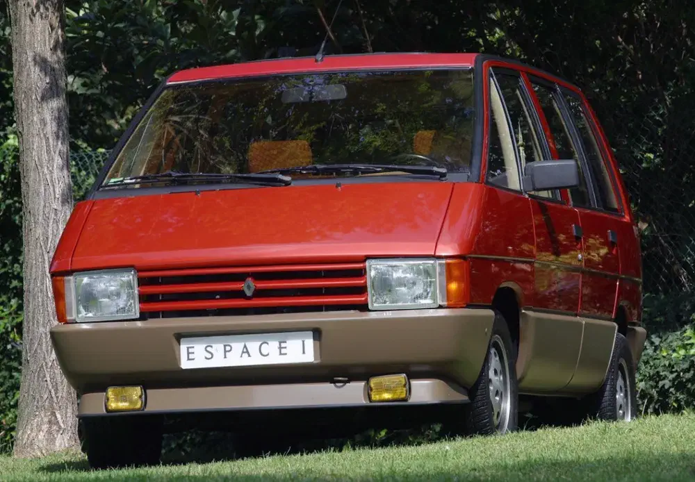 Renault Espace rouge des années 80 garé sur l'herbe, emblématique et spacieux.