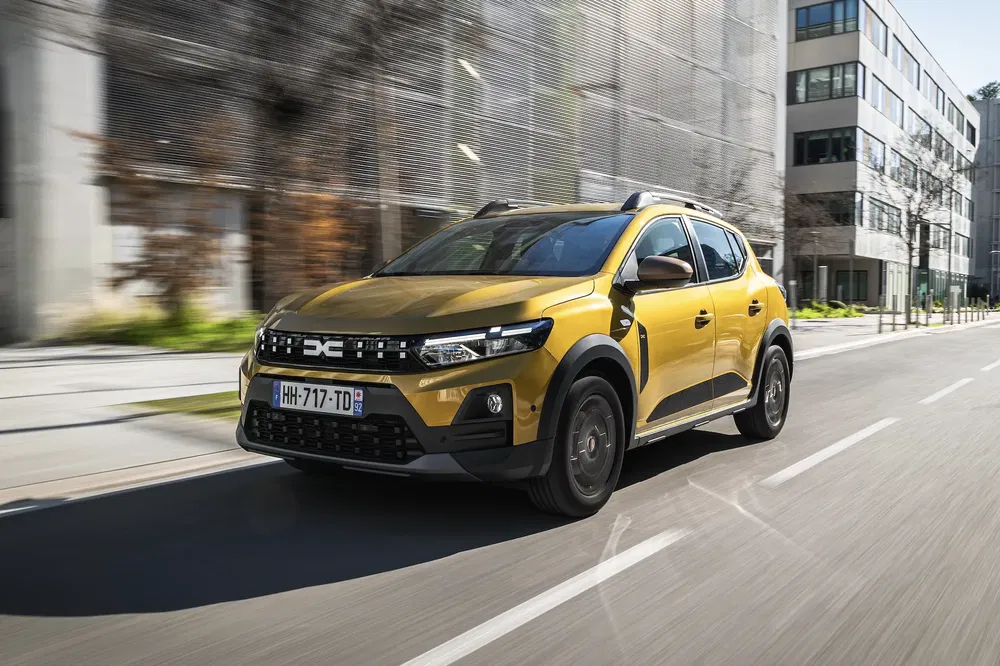 Gele Dacia Sandero Stepway rijdt door stedelijke straat, zijaanzicht.