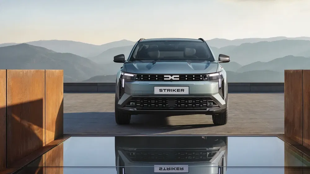 Grijze Dacia Striker auto op moderne brug met bergen op de achtergrond.