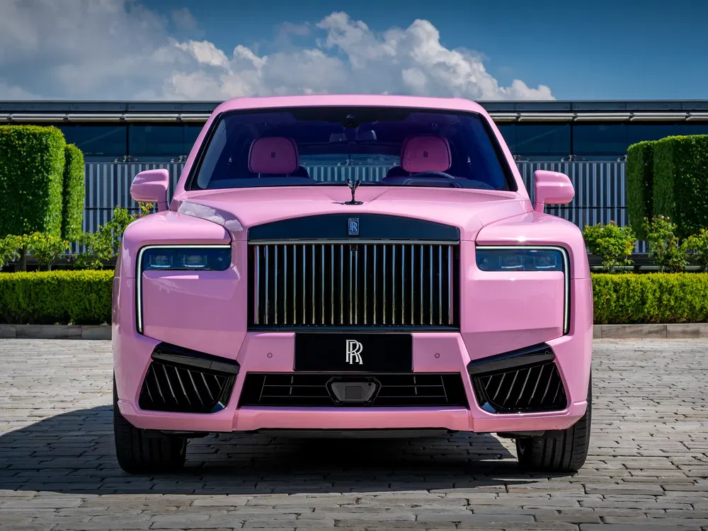Rolls-Royce rose avec calandre emblématique sur fond de jardin élégant.