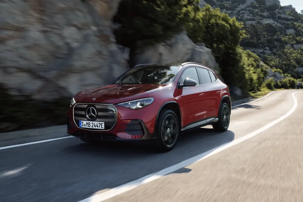 Rode Mercedes-Benz EQA rijdend op een kronkelige bergweg omringd door groene natuur.