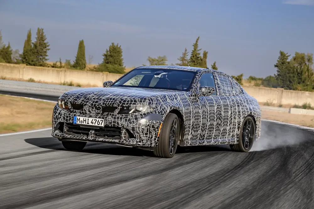 BMW camouflé en test sur piste, penchant dans un virage avec un numéro d'immatriculation.