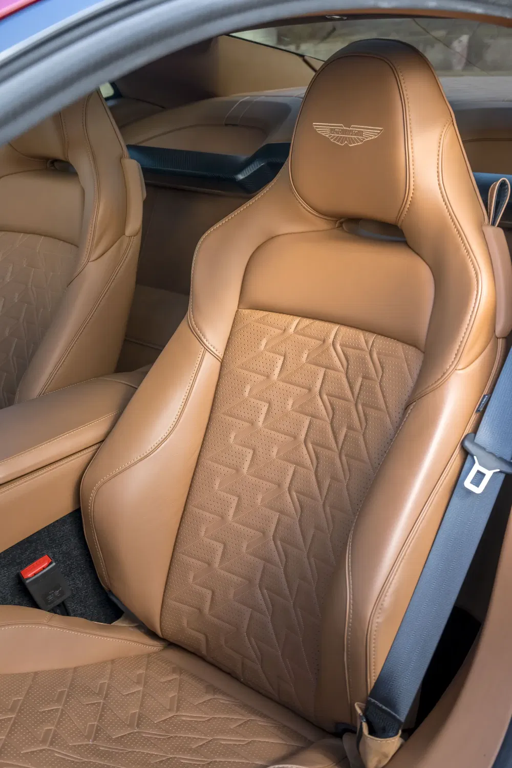 Siège en cuir marron Aston Martin avec motif géométrique distinctif et logo embossé.
