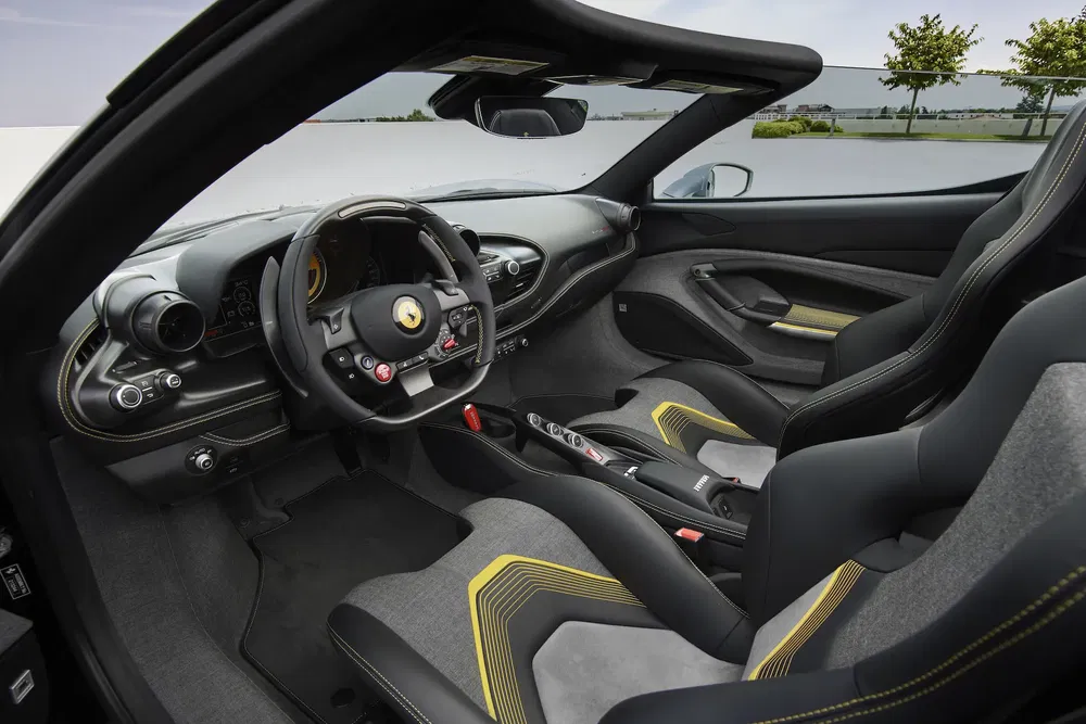 Intérieur luxueux d'une Ferrari avec volant sport et sièges en Alcantara gris et jaune.