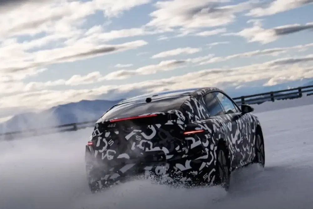 Voiture camouflée Kia EV6 roulant sur la neige lors d'un test hivernal sous ciel nuageux.