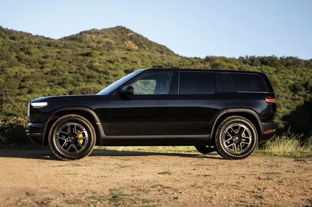 SUV Rivian R1S noir stationné devant un paysage montagneux verdoyant.