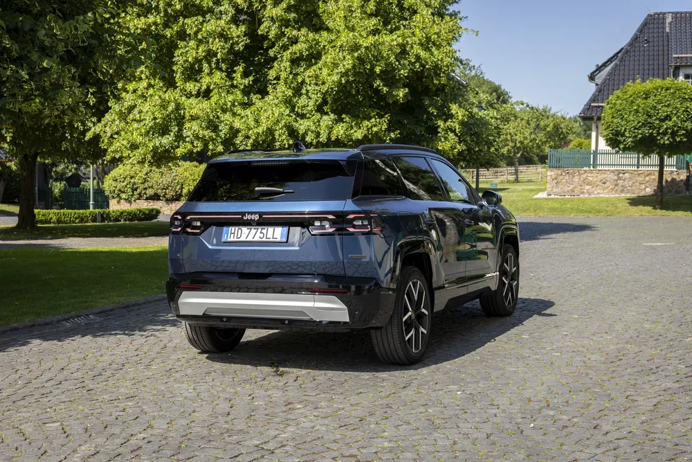 Jeep Grand Cherokee noir garée sur une allée pavée, entourée d'arbres et de maisons.