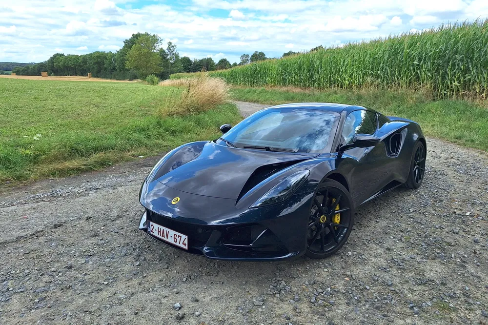 Zwarte Lotus Emira geparkeerd op een grindweg omringd door groene velden.