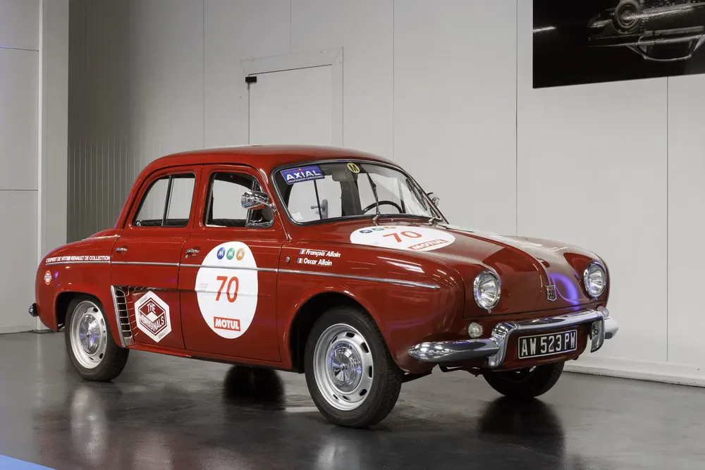 Voiture classique Renault Dauphine rouge avec autocollants de course dans un showroom.