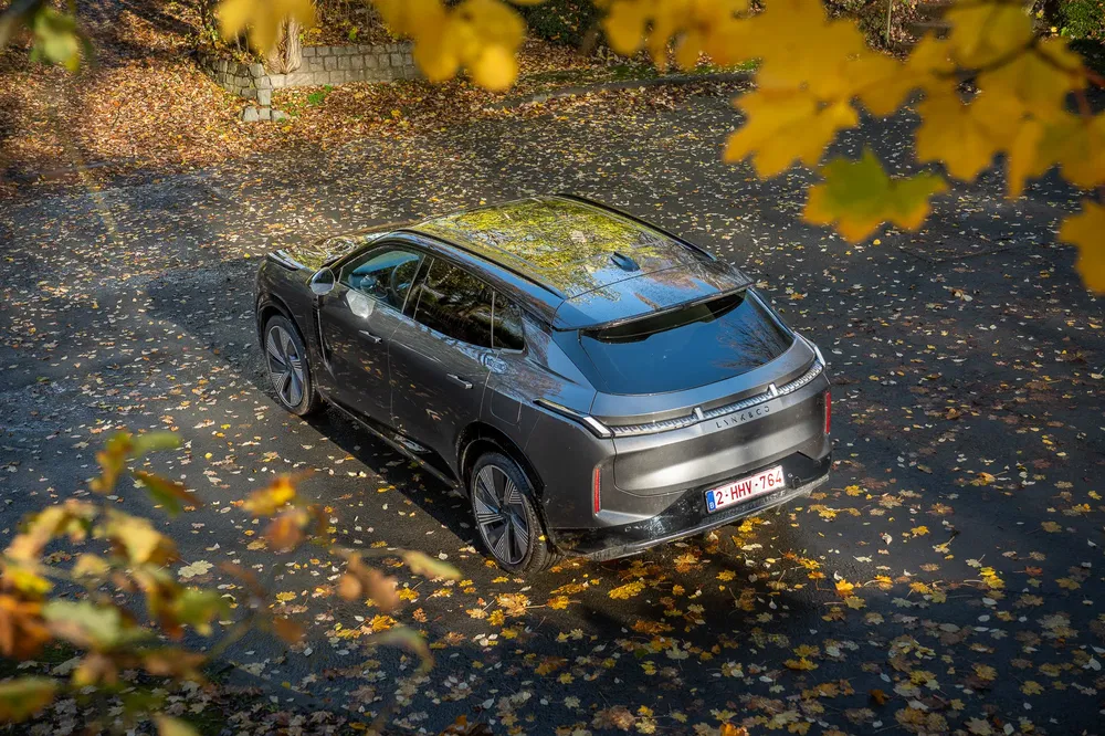 Lynk & Co SUV gris stationné sur route couverte de feuilles d'automne, vue de dessus.