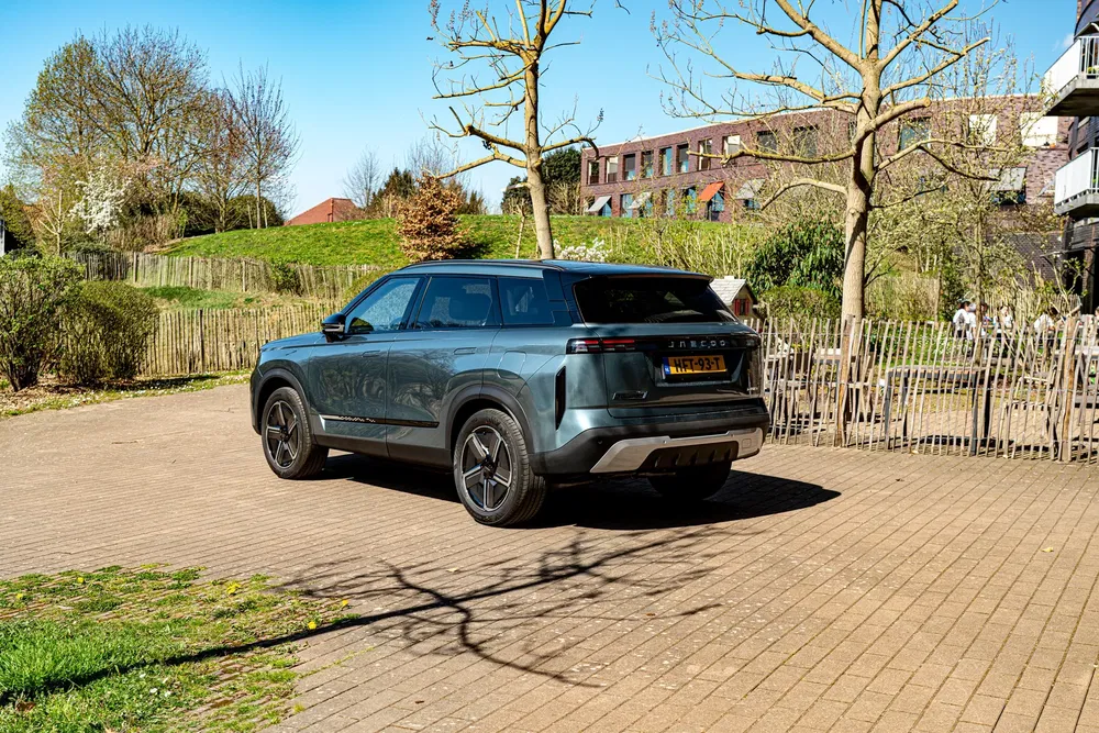 Moderne SUV geparkeerd op een geplaveide oprit, met bomen en gebouwen op de achtergrond.
