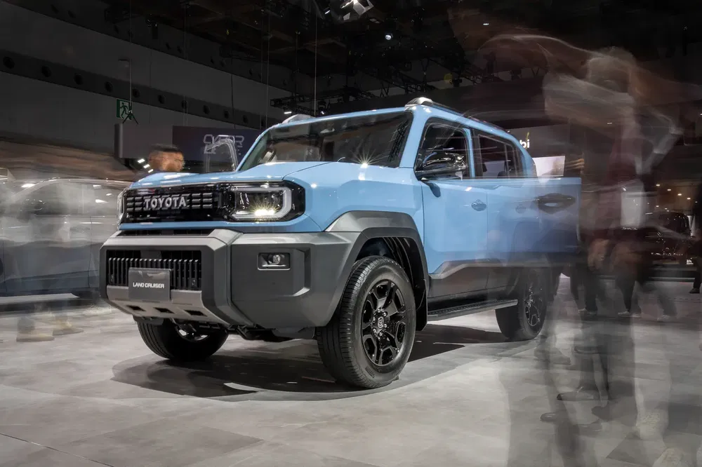 Blauwe Toyota Land Cruiser gepresenteerd op autoshow, met wazige bezoekers in beweging.