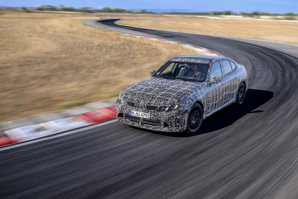 Prototype de voiture BMW camouflée réalisant une courbe sur une piste de course.