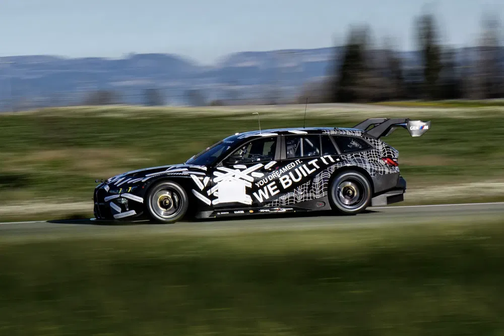 BMW M3 Touring racet op circuit, met opvallend camouflageontwerp en krachtige achtervleugel.