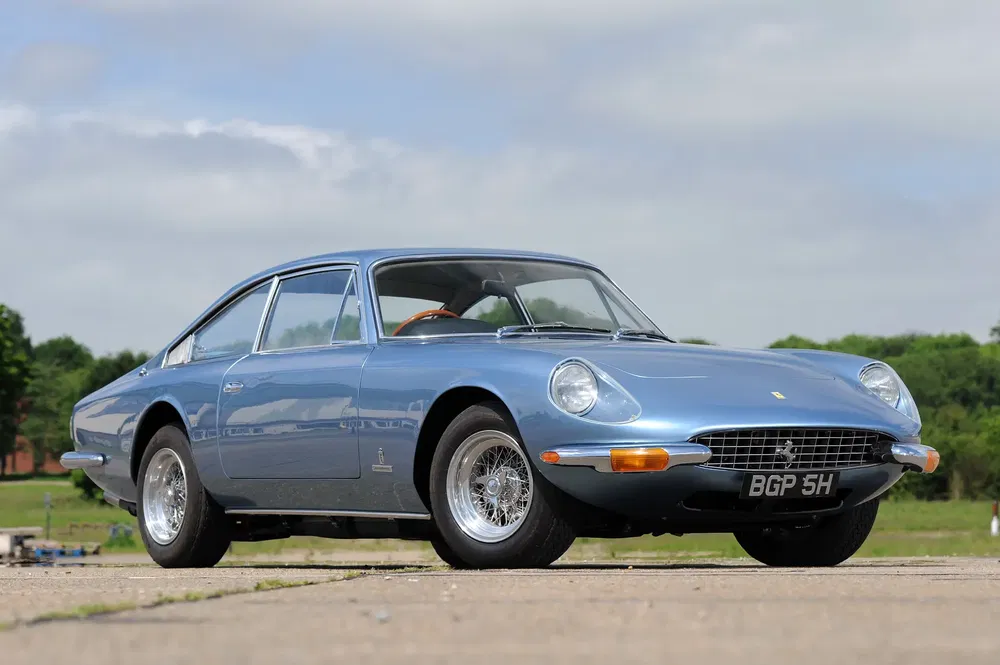Blauwe Ferrari 365 GT 2+2, elegante klassieker op een geplaveide weg in het platteland.