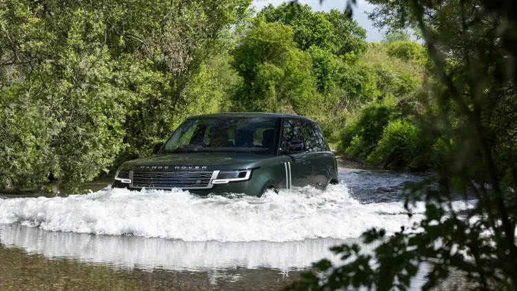 SUV Range Rover naviguant à travers un cours d'eau entouré de verdure dense.