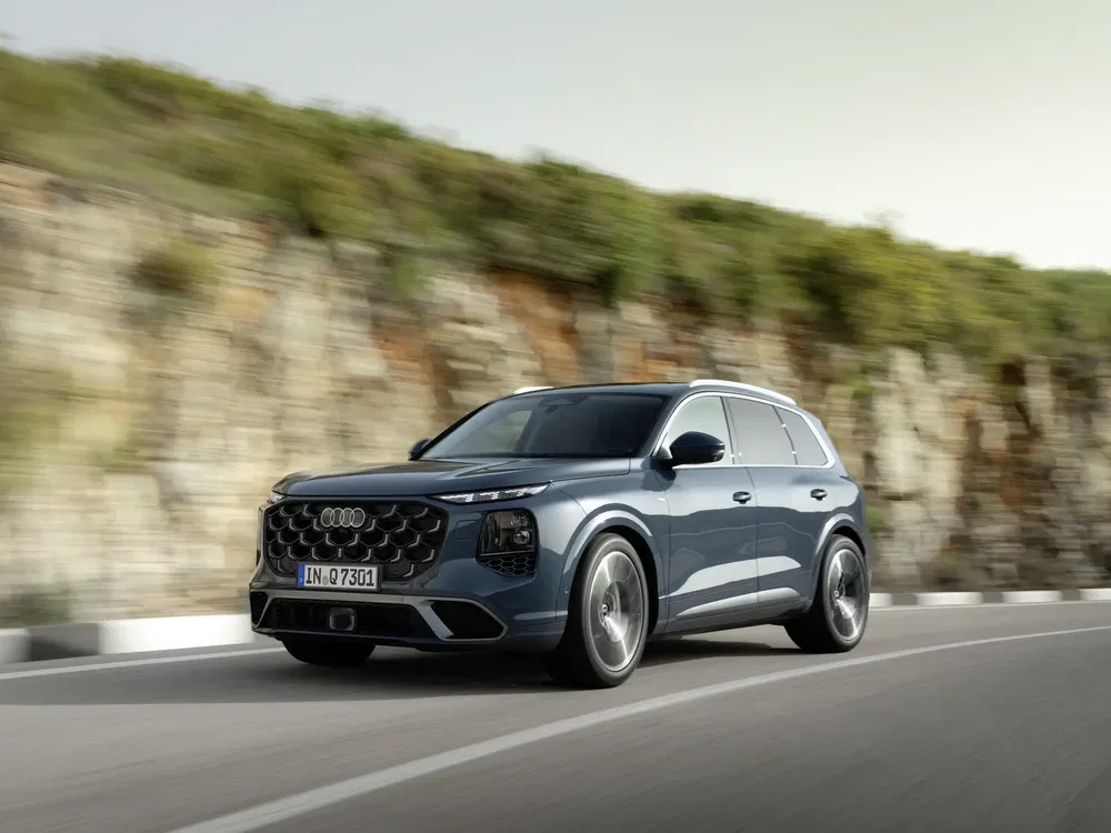Audi Q7 bleu sur route sinueuse devant un mur rocheux.