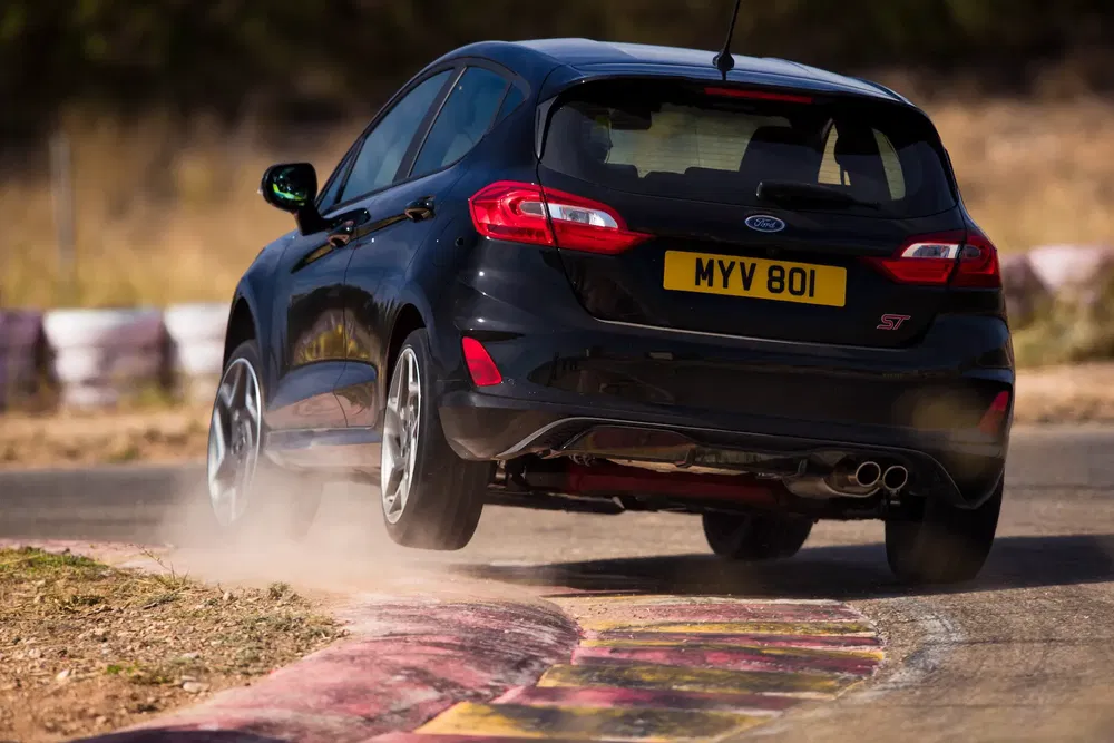 Ford Fiesta ST noir en virage serré sur une piste, pneus arrière soulevés.