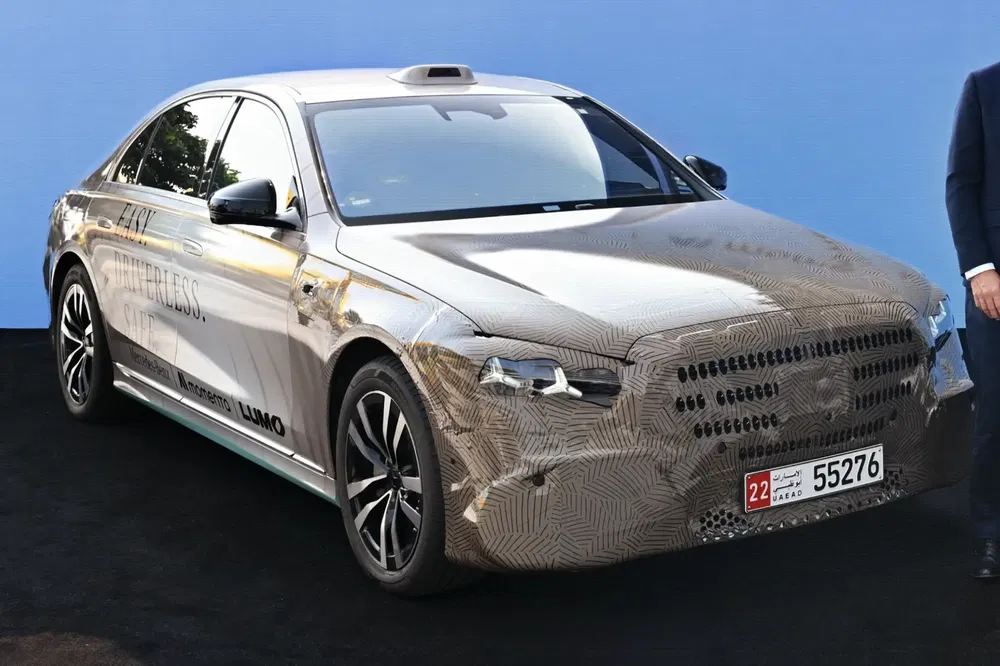 Berline autonome Mercedes sous camouflage sur fond bleu, équipée de capteurs technologiques avancés.