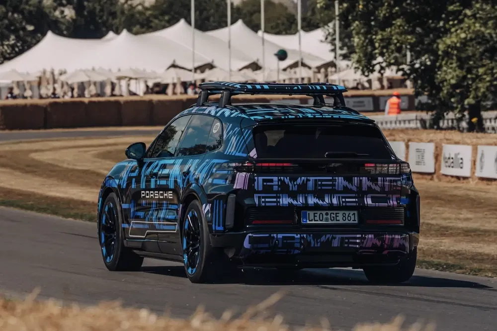 Porsche Cayenne prototype bleu sur un circuit avec tentes en arrière-plan.