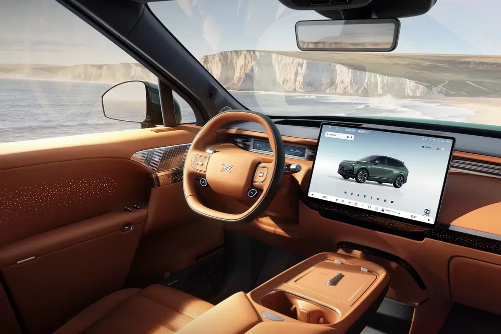 Intérieur de voiture XPeng P7 avec écran tactile, finitions en cuir marron, vue sur la mer.