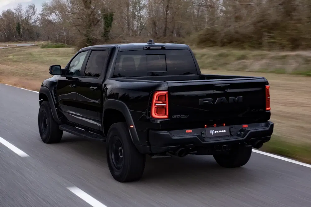 Zwarte Ram TRX pick-up rijdt op een weg met bomen op de achtergrond.