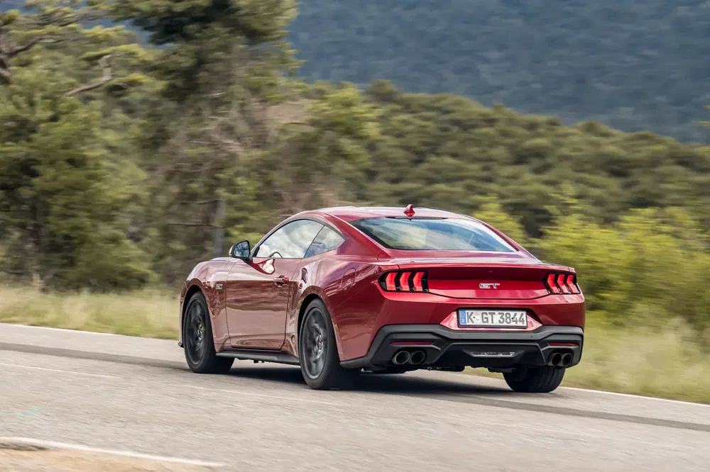 Rode Ford Mustang GT op bochtige weg, krachtige achterkant en sportief ontwerp.