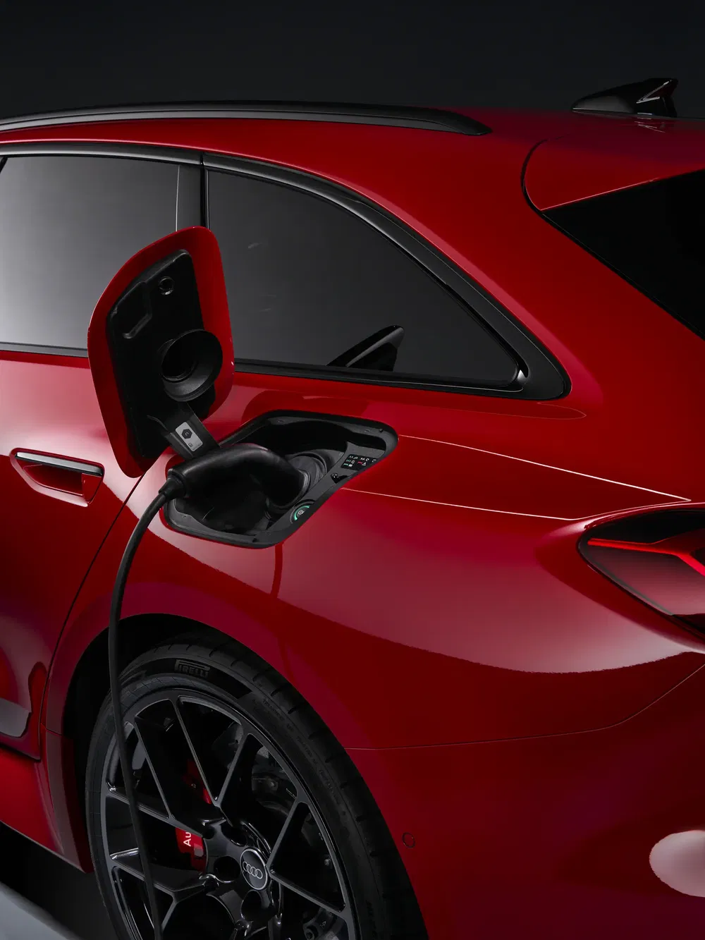 Rode Audi aan elektrische lader, zij-achteraanzicht met aangesloten kabel, kenmerkende zwarte velg.