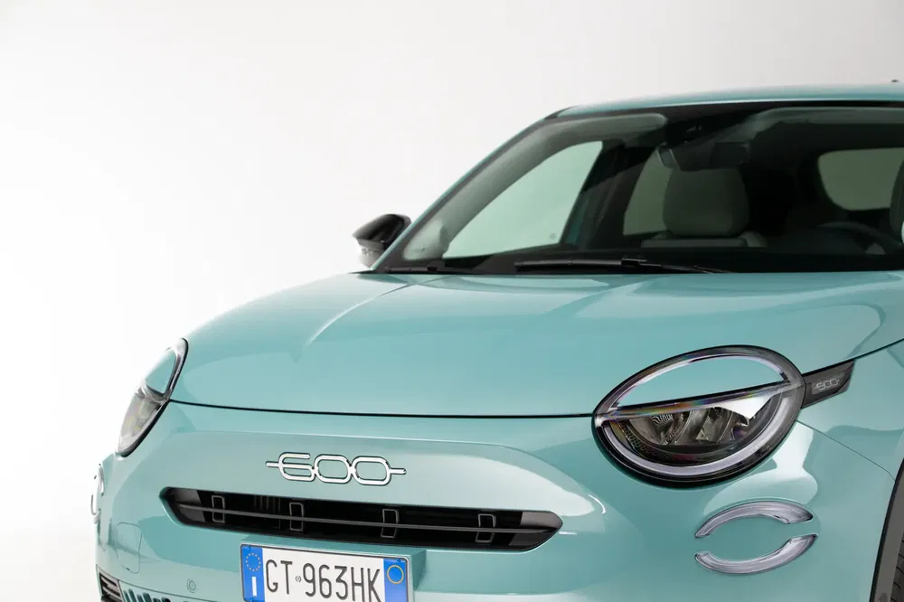 Halve voorzijde van een turquoise Fiat 600 met Italiaanse kentekenplaat en moderne koplampen.