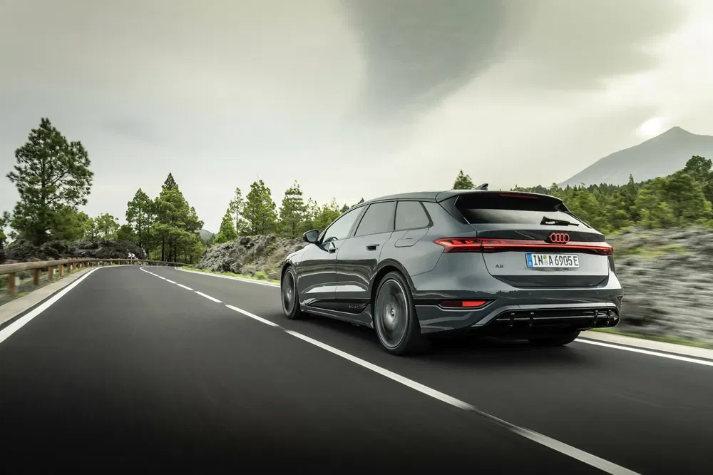 Audi A6 e-tron gris sur route sinueuse entourée de paysages forestiers.