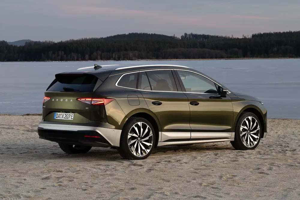 Skoda Enyaq iV SUV vert sur plage, vue arrière avec lac et forêt.