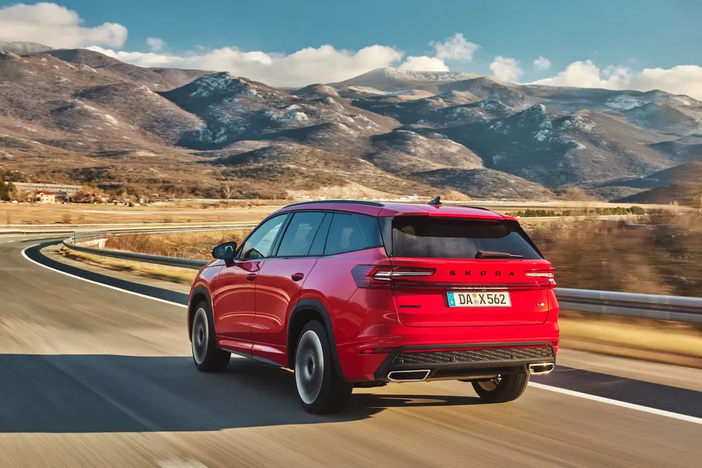 SUV Skoda rouge sur route montagneuse ensoleillée, paysage naturel en arrière-plan.