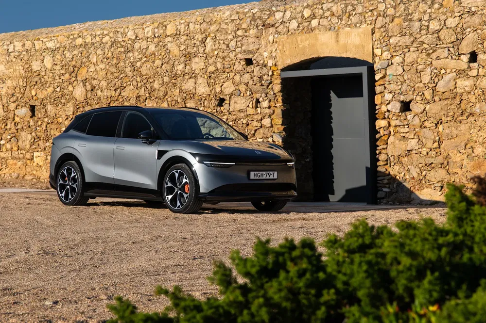 Voiture électrique stationnée devant un mur en pierre sous un ciel bleu clair.