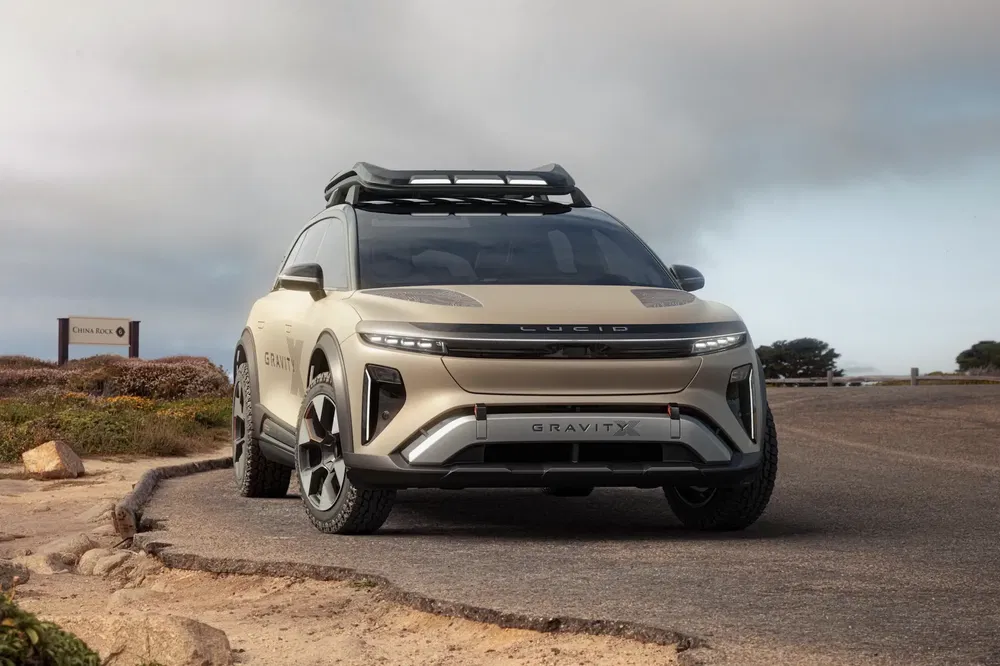 Lucid Gravity SUV beige sur route côtière, design moderne et toit avec galerie.